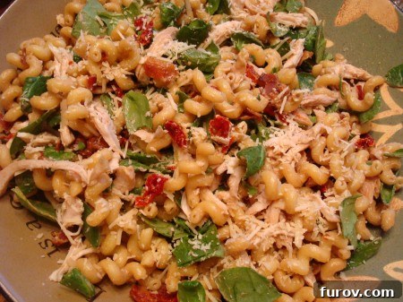 Chicken Pasta Salad with Sun-Dried Tomatoes, Fresh Spinach, and Crispy Bacon 2 A vibrant pasta salad with spinach and sun-dried tomatoes mixed throughout, served in a light blue bowl.