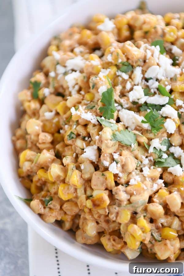 Zesty Mexican Street Corn Salad 6 A pristine white bowl overflowing with creamy Mexican street corn salad, generously topped with fresh cilantro and a bright lime wedge, ready to be enjoyed.