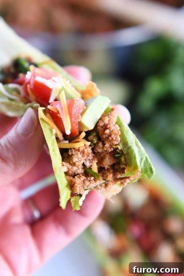 Vibrant Veggie Turkey Lettuce Tacos 11 A hand holding a veggie turkey taco lettuce wrap with a bite taken out, highlighting the delicious layers of filling and toppings.
