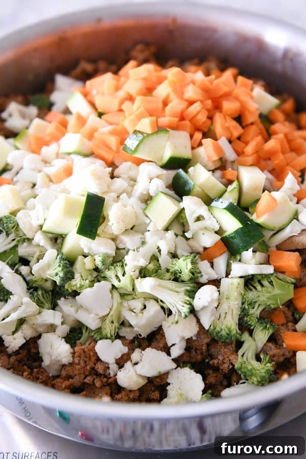 Vibrant Veggie Turkey Lettuce Tacos 6 A mix of chopped carrots, zucchini, broccoli, and cauliflower being added to the seasoned ground turkey in a skillet.