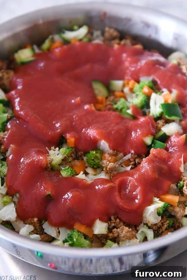 Vibrant Veggie Turkey Lettuce Tacos 8 Tomato sauce being stirred into the cooked ground turkey and vegetable mixture in a skillet.