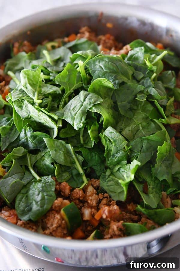 Vibrant Veggie Turkey Lettuce Tacos 9 Fresh spinach leaves being added to the simmering taco filling, ready to be wilted.