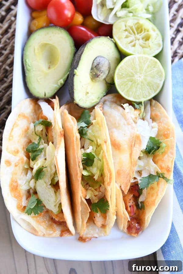 Golden Crunch Shrimp Tacos 9 A top-down view of a white tray featuring a selection of crispy baked shrimp tacos, alongside a perfectly halved avocado and lime wedges, showcasing fresh garnishes.