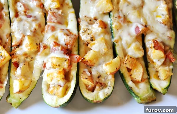 Several golden-brown stuffed baked zucchini halves neatly arranged on a white serving platter, ready to be enjoyed.