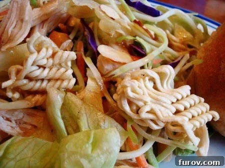 A beautifully plated Asian chicken salad, showcasing vibrant greens, shredded chicken, and crunchy ramen noodles with almonds.