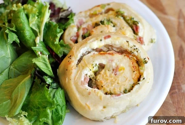 Two golden-brown stuffed pinwheel rolls next to a fresh bed of lettuce on a pristine white plate.