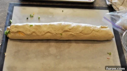 The bread dough has been completely rolled into a smooth, even log, with the seam carefully pinched to seal in the filling.