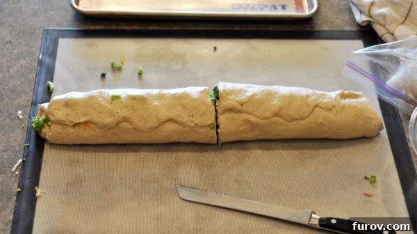 The perfectly rolled dough log is cut in half, revealing the vibrant spiral layers of ham, broccoli, and cheese filling inside.