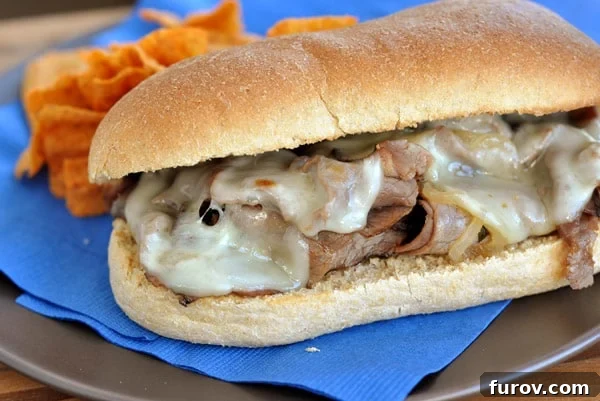 Delicious cheesesteak sub sandwich with melted provolone cheese, caramelized onions, and tender beef, perfectly nestled on a fresh sub roll, resting on a blue napkin.