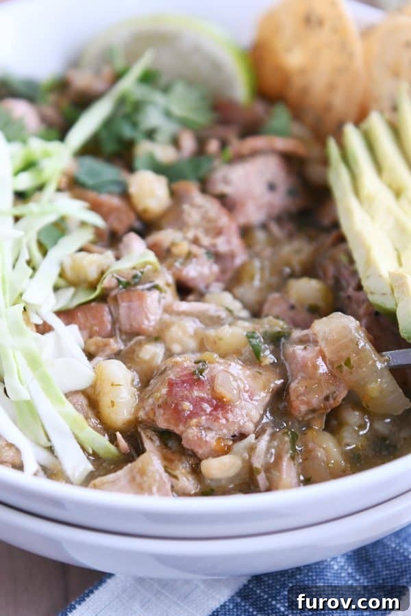 Seasoned pork, hominy, broth, cabbage, avocado in a white bowl, showcasing the rich textures and colors of the posole ingredients.