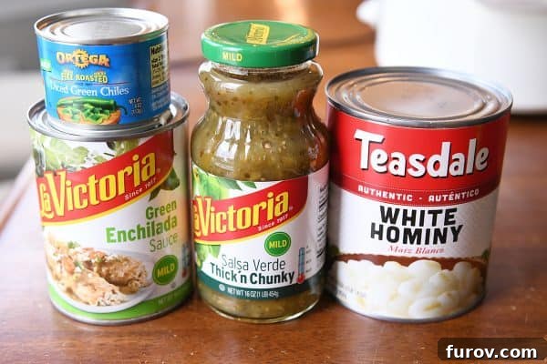 Selection of canned ingredients: green enchilada sauce, diced green chiles, thick and chunky salsa verde, and white hominy, highlighting the convenience of pantry staples.