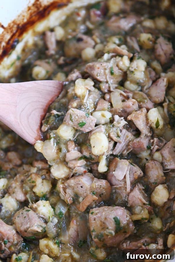 A wooden spoon scooping slow cooker posole from a pot, showing the rich, chunky texture of the stew.