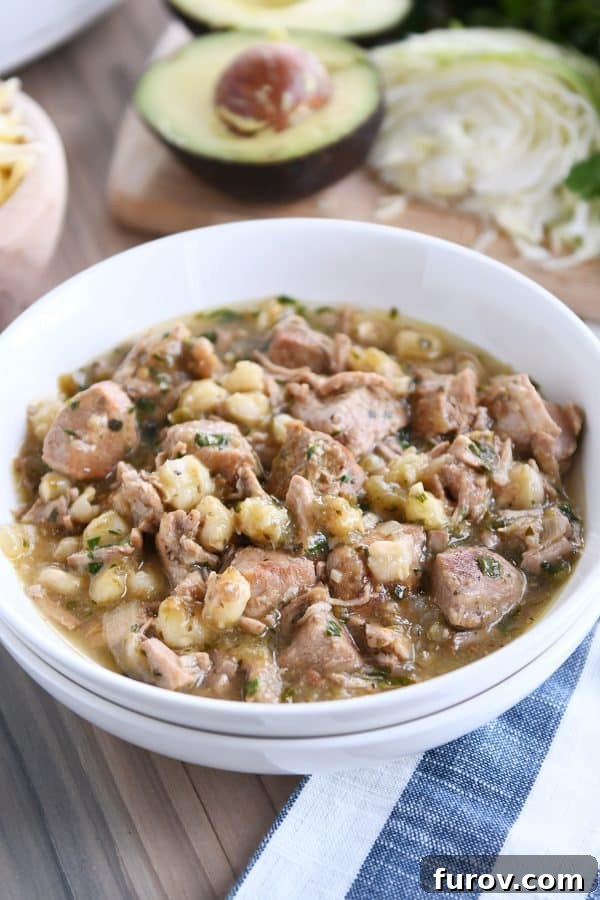 White bowl with slow cooker posole garnished with fresh toppings on a rustic wood board, ready to be enjoyed.