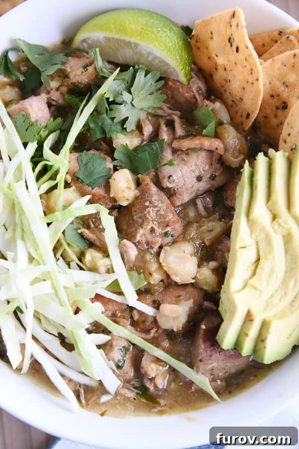 Close-up of a spoonful of posole, showing tender pork, hominy, fresh cilantro, avocado, and cabbage, highlighting the texture and freshness of the dish.