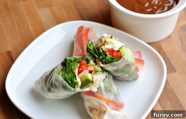 A spring roll cut in half, revealing its colourful interior, resting on a whole spring roll.