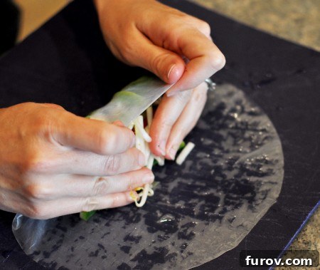 The bottom edge of the rice paper wrapper being folded over the filling.