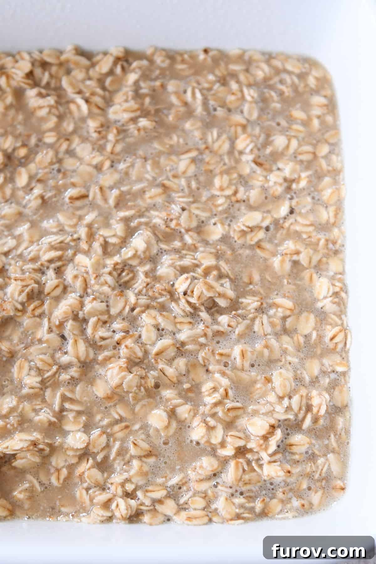 The unbaked Amish baked oatmeal mixture neatly arranged in a white ceramic baking dish, ready for refrigeration or immediate baking.