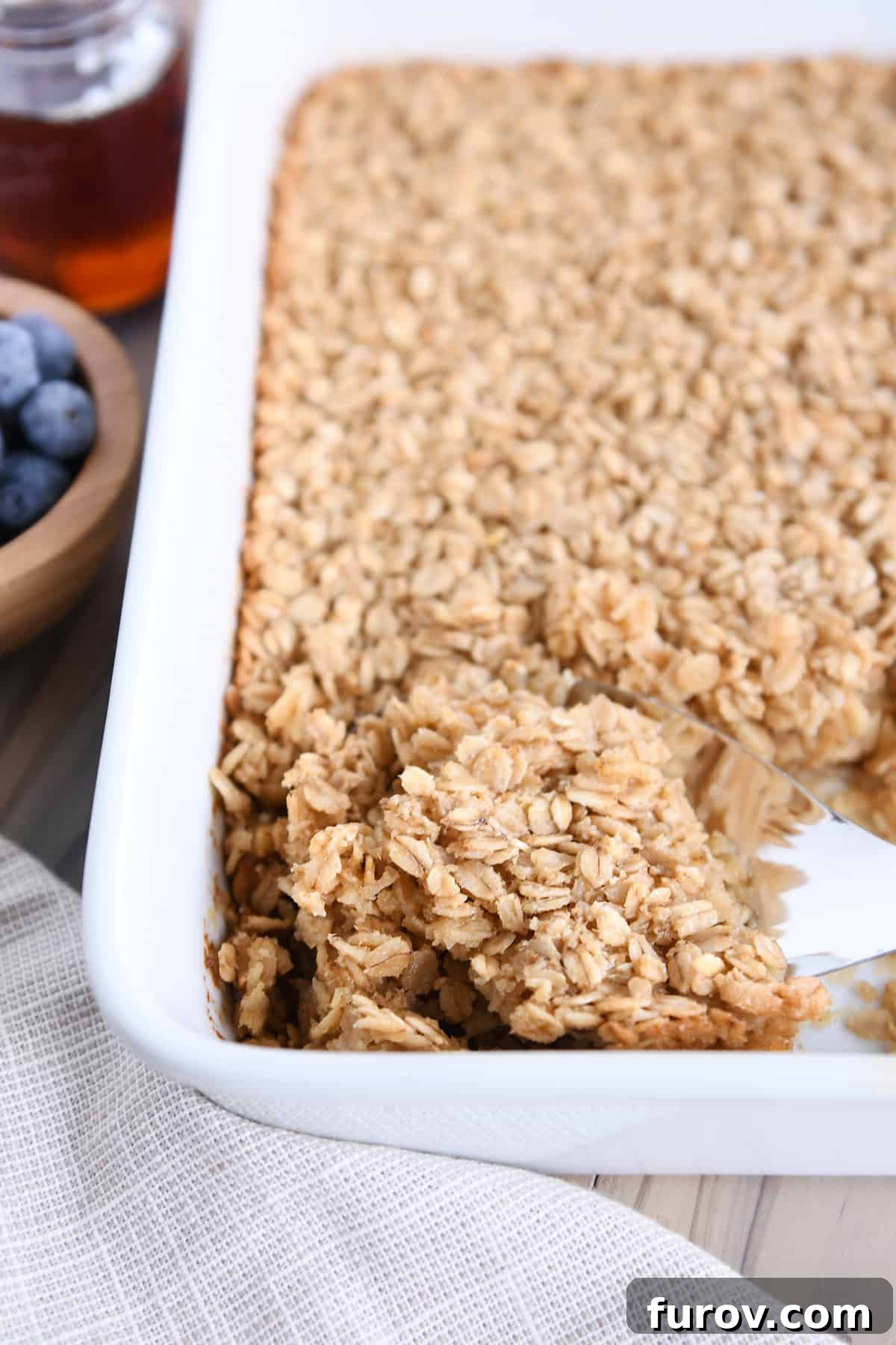 A serving spoon gracefully scooping a portion of warm, baked oatmeal from a white baking dish, showcasing its inviting texture.