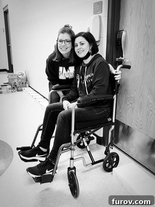 A woman in a wheelchair, Holli, with a friend standing lovingly by her side, depicting support and companionship during difficult times.