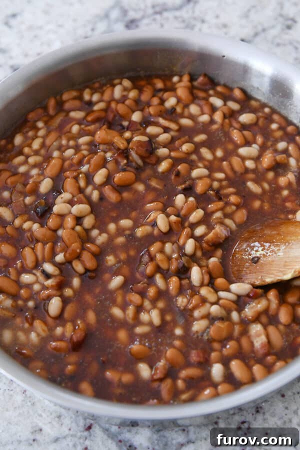 Close-up shot of baked beans bubbling in a shallow metal pan, showcasing their rich, saucy texture and readiness to be served.