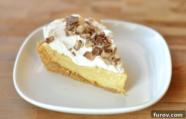 Slice of pudding pie with graham cracker crust, a golden pudding layer, and a generous topping of whipped cream and toffee bits.