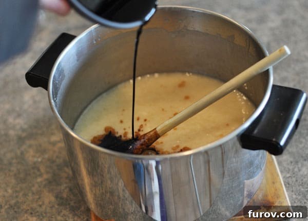 Fudge mixture in a pot with vanilla extract being poured in, creating aromatic steam.