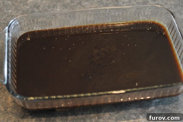 Dark colored fudge mixture settling in a glass 9x13 inch baking pan, left to cool undisturbed.