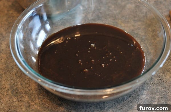 Dark colored fudge mixture in a glass bowl, ready for beating to achieve creamy consistency.