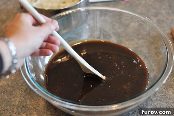 Dark fudge mixture in a glass bowl being stirred by a wooden spoon, showing a lighter color and thicker consistency.