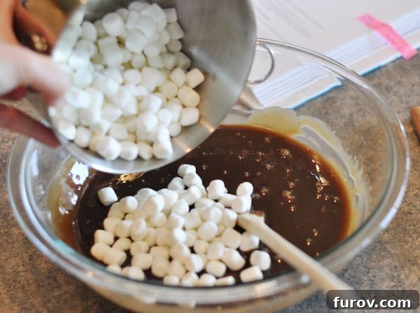 Fudge mixture in a glass bowl with marshmallows being gently dumped in for mixing.