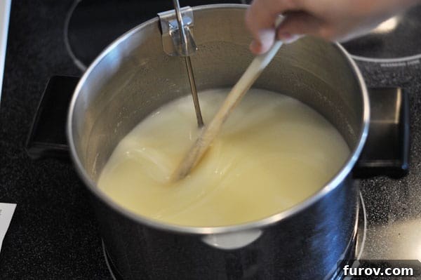 Sugar mixture dissolving in a large pot, with a wooden spoon and candy thermometer. The ingredients are just starting to combine.