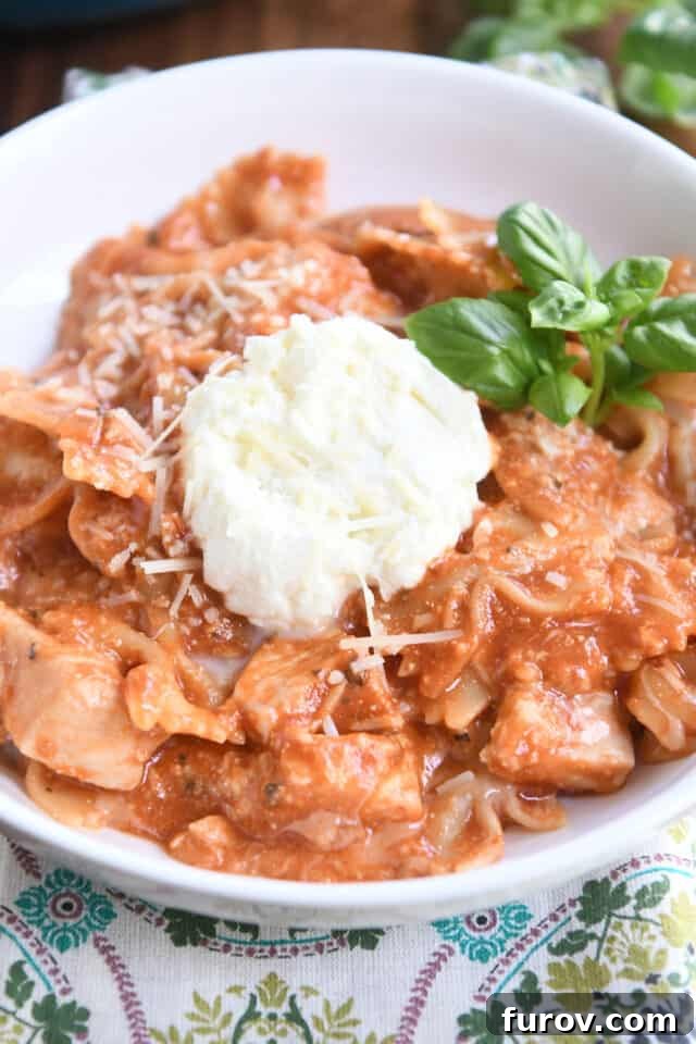 Serving of chicken lasagna in white bowl with spoonful of ricotta and fresh basil leaves, ready to be enjoyed.