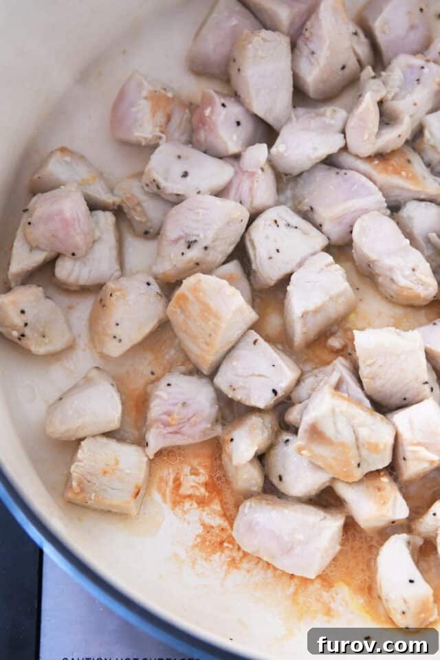 Chicken cubes cooking in oil in cast iron pot, searing to perfection.