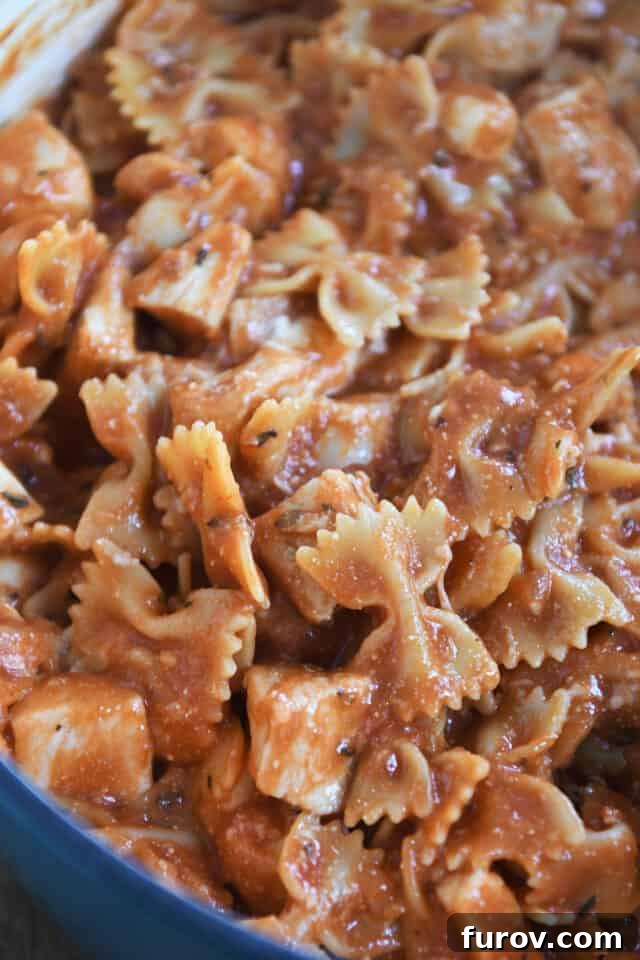 Cooked bowtie pasta and chicken in a rich tomato sauce, served in a blue pot, ready to be dished out.