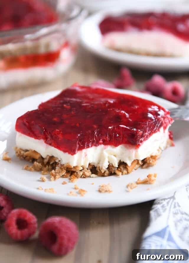 A perfect square of Raspberry Pretzel Jello resting on a white plate, with a corner gently removed, showcasing the distinct, vibrant layers.