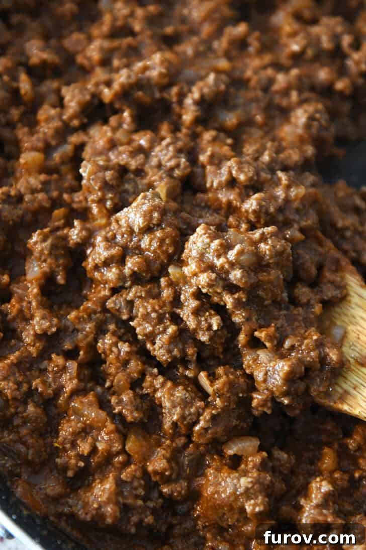 Top-down view of a skillet filled with rich, seasoned taco meat, with a wooden spoon scooping out a portion, illustrating its perfect texture and consistency.