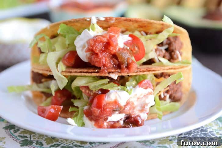 Two perfectly stacked ground beef tacos, generously filled and garnished, presented on a simple white plate, ready to be enjoyed.