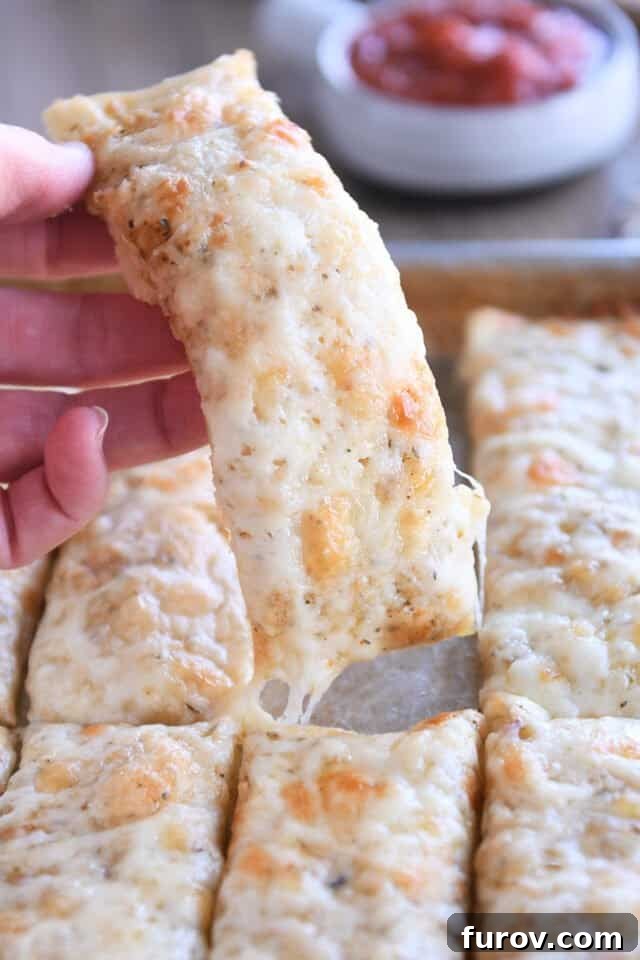 Holding one cheesy breadstick, showcasing its golden crust and melted cheese.