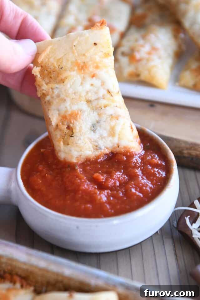 Dipping cheesy breadstick into marinara sauce, highlighting its perfect texture and appeal.