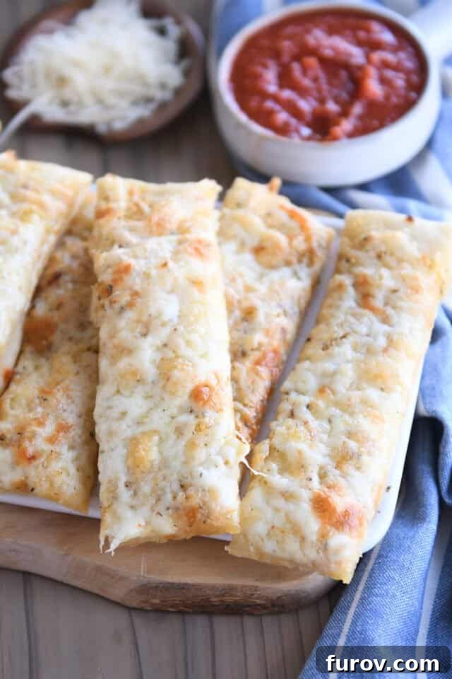 Four cheesy breadsticks arranged on a rustic wood cutting board.