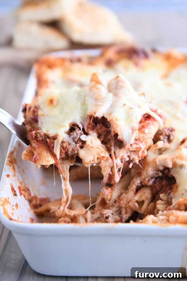 Make Ahead Freezer Friendly Cheesy Weeknight Pasta Bake 2 Scooping serving of weeknight pasta bake out of white 9X13-inch pan.