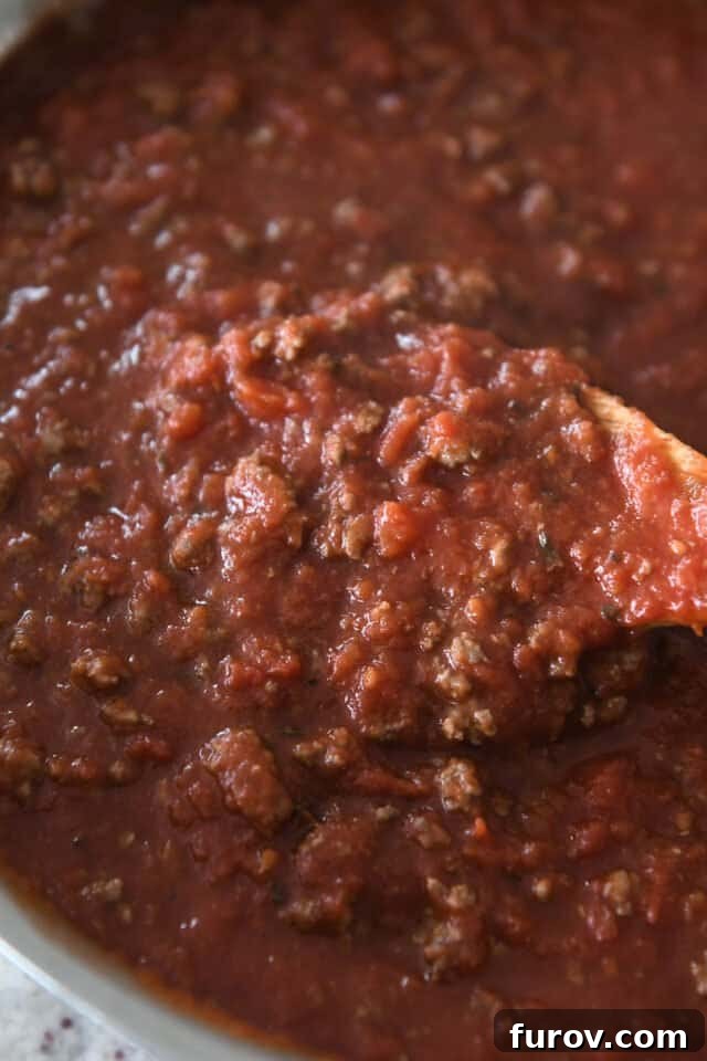 Make Ahead Freezer Friendly Cheesy Weeknight Pasta Bake 3 Wooden spoon scooping red sauce with ground beef in stainless pan.