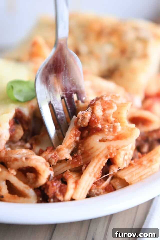 Make Ahead Freezer Friendly Cheesy Weeknight Pasta Bake 7 Fork taking a bite of penne noodles with red sauce on white plate.