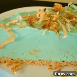 A perfectly sliced Frozen Key Lime Pie garnished with toasted coconut and fresh lime wedges.