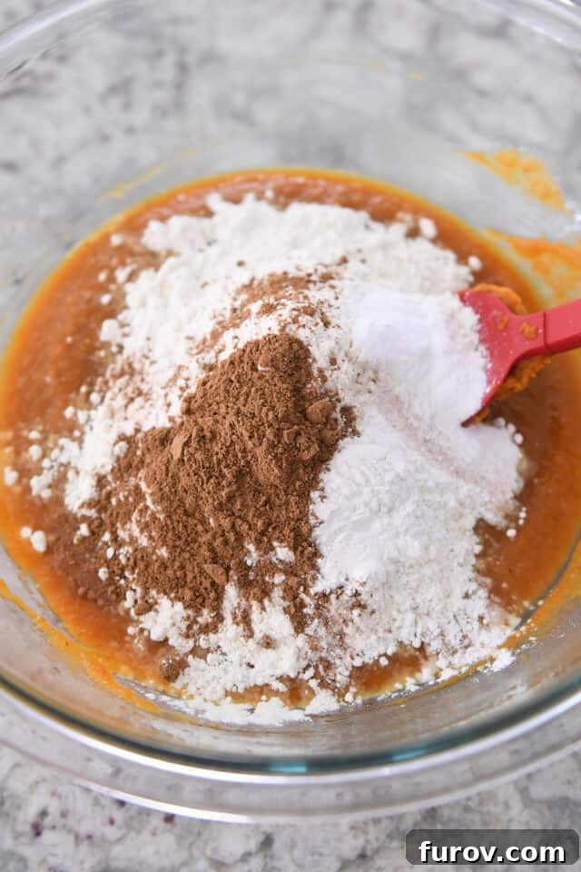 Cinnamon, flour, and baking soda neatly arranged in a glass bowl, prepared to be mixed into a creamy pumpkin batter, illustrating careful ingredient preparation.