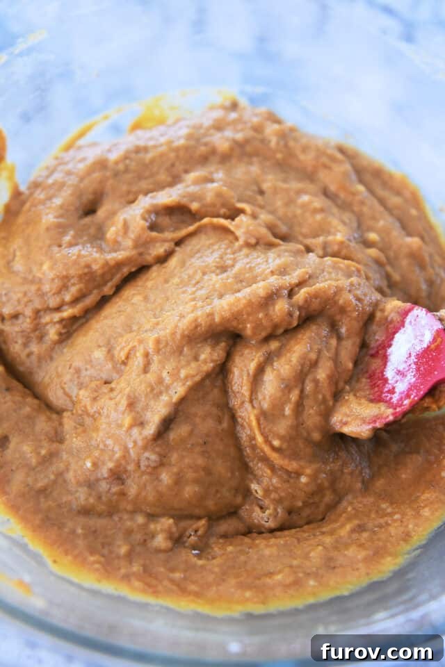 A large glass bowl filled with smooth, vibrant orange pumpkin muffin batter, perfectly mixed and ready for the next step in baking.