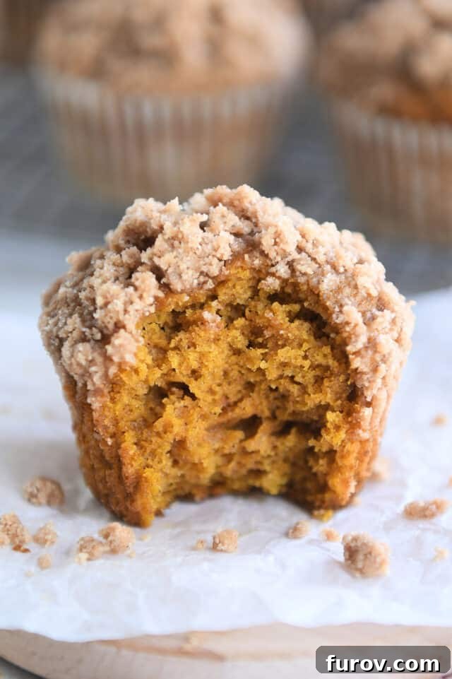 A delicious pumpkin muffin with a crunchy streusel topping, showcasing a perfect bite taken out to reveal its soft, spiced interior, resting on white parchment paper.