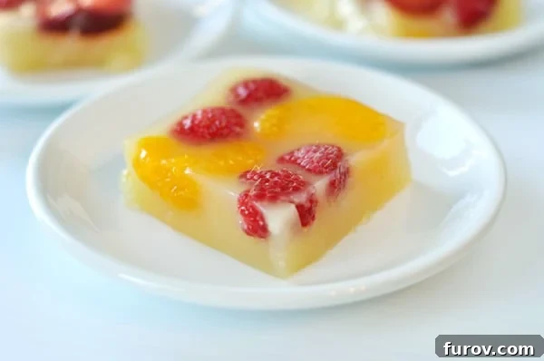 Bright and Bubbly Homemade Orange Jello 2 A vibrant slice of homemade sparkling orange gelatin adorned with fresh raspberries and juicy mandarin orange segments, presented on a pristine white plate.