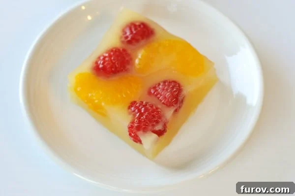 Bright and Bubbly Homemade Orange Jello 3 Top-down view of glistening homemade sparkling orange gelatin, studded with whole raspberries and vibrant mandarin orange slices, showcasing its inviting texture.