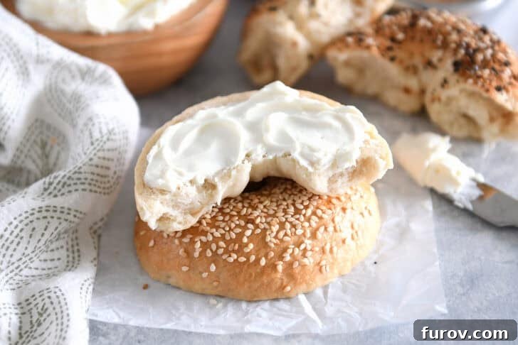 One half of a fresh homemade bagel slathered with creamy cream cheese on top of a sesame seed coated half.